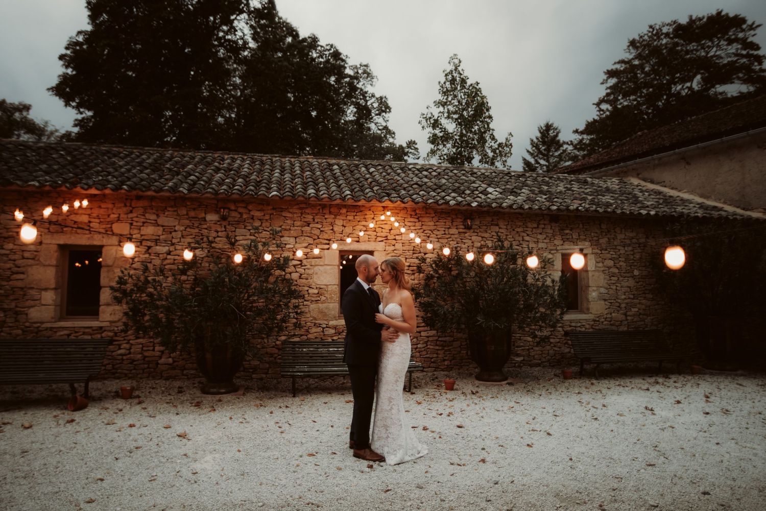 Intimate wedding moment captured under string lights in a rustic stone courtyard.