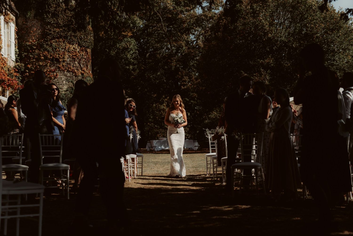 A wedding ceremony setup with white chairs under trees at sunset.
