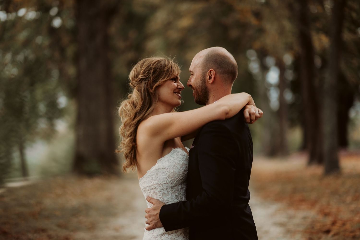 Intimate wedding moment captured in warm autumn light beneath tall trees.