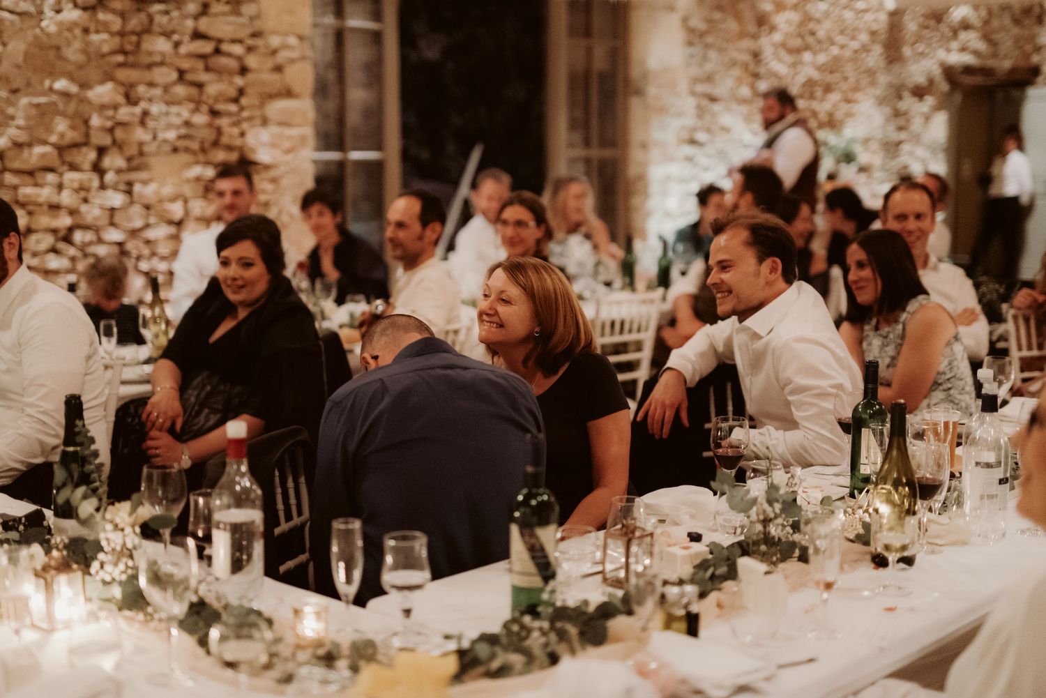 Wedding guests seated at long dinner tables in a rustic stone venue enjoying the reception.