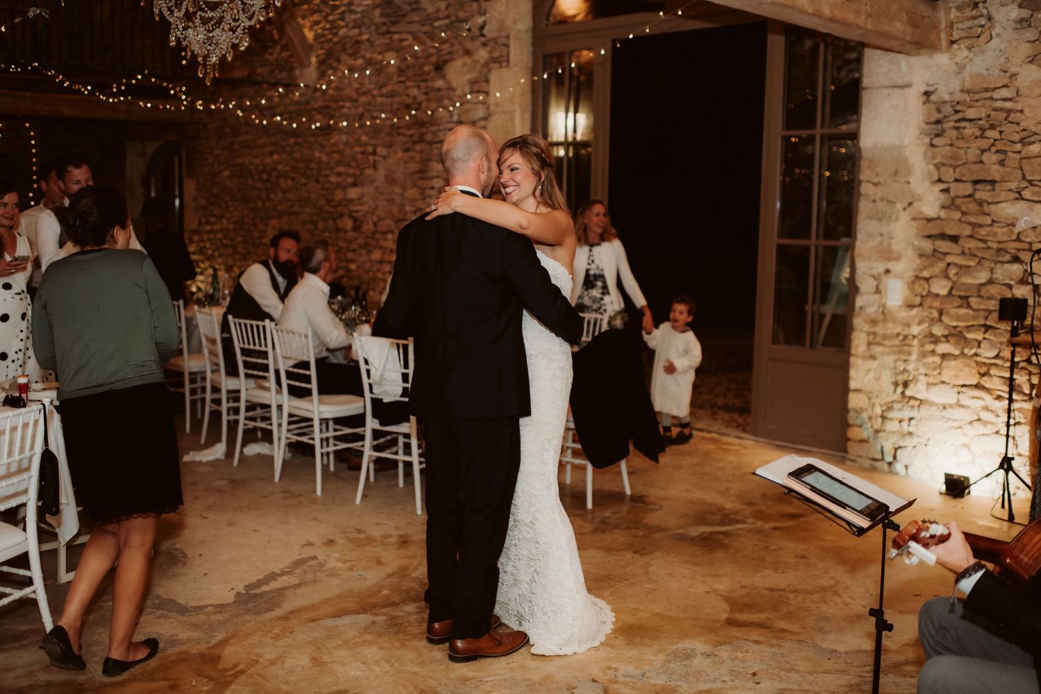 A couple shares their first dance in an elegant stone-walled venue with string lights.