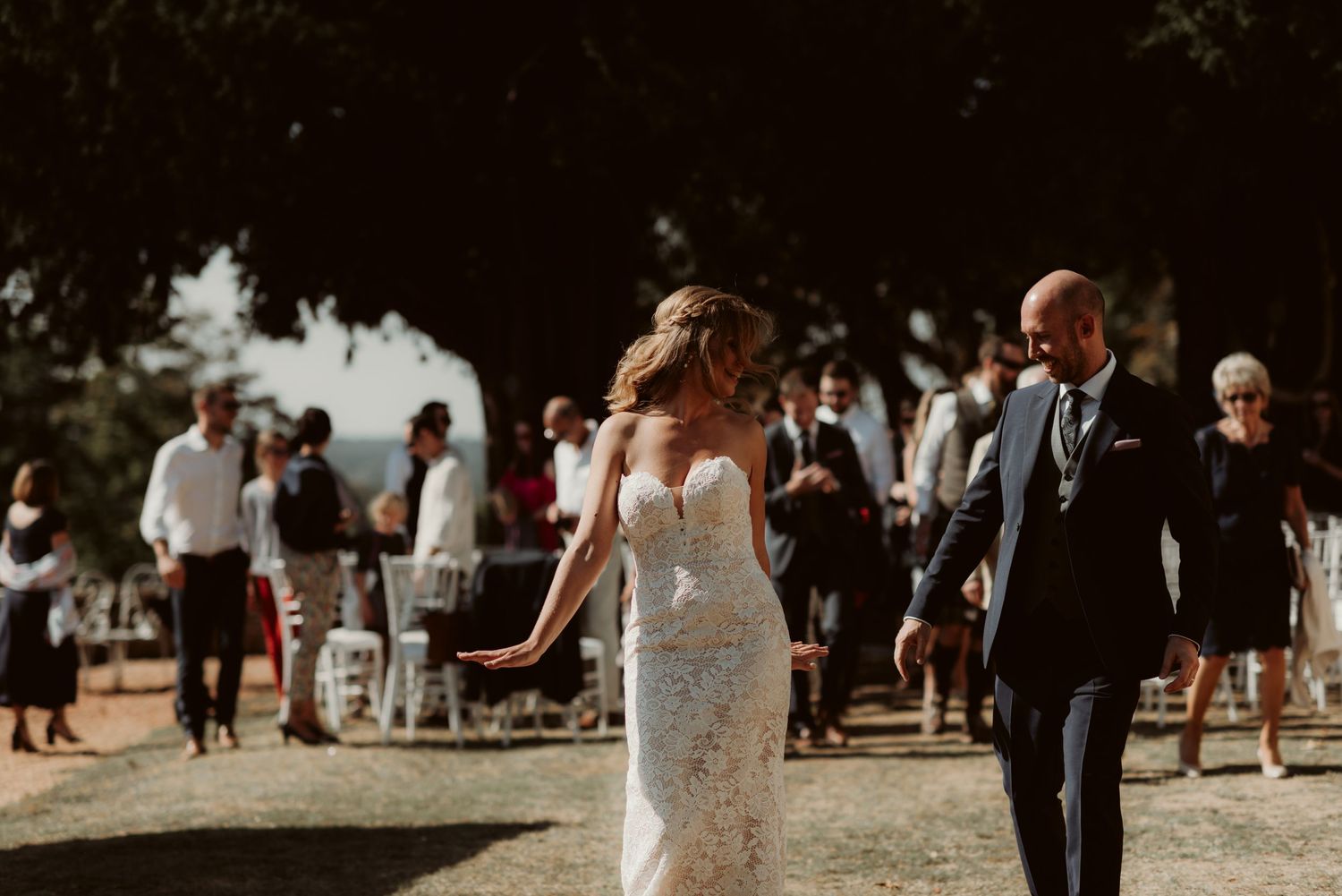 Newlyweds celebrate during their outdoor ceremony with guests and white chairs in the background.