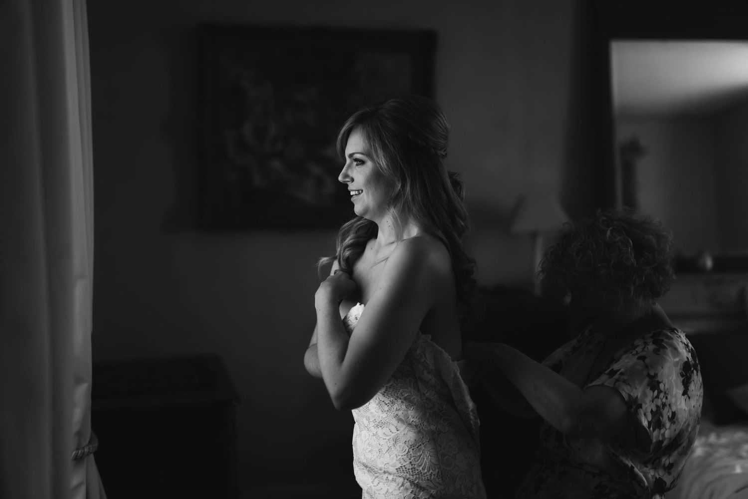 Black and white photo of wedding dress preparation in dimly lit room.