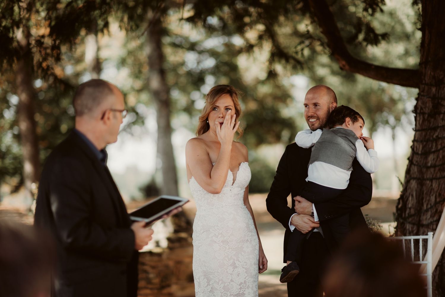 A candid wedding ceremony moment showing reactions during the vows under forest trees.