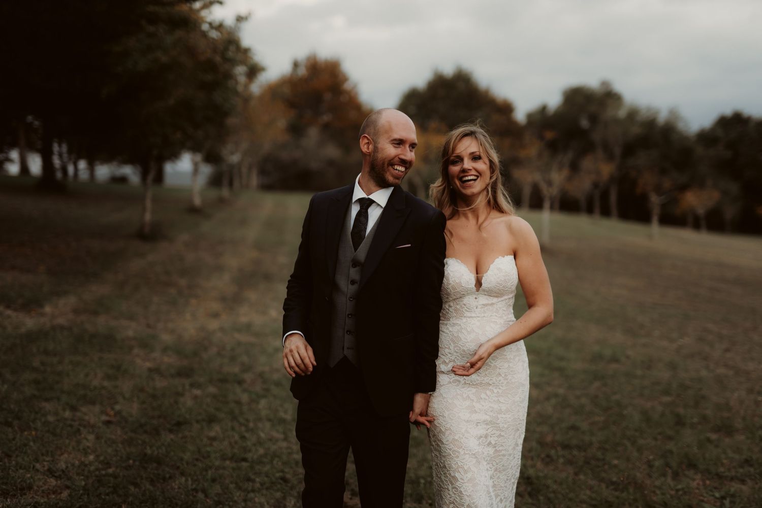 A couple shares a joyful moment in their wedding attire on a hillside.