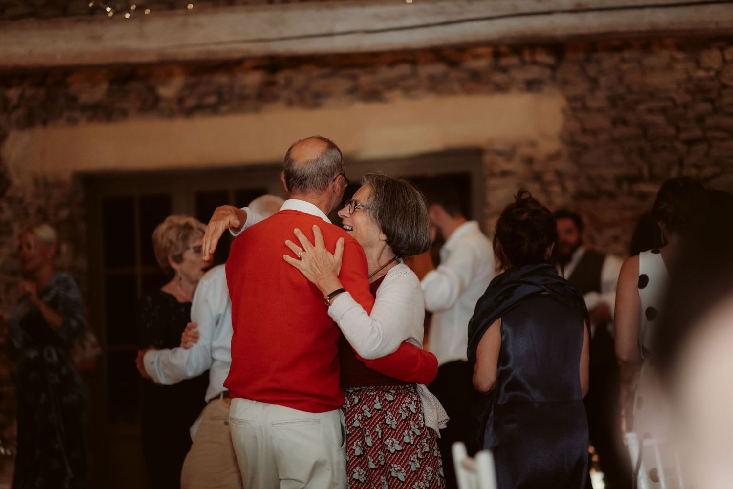 People dancing at an intimate gathering in a warmly lit stone interior.