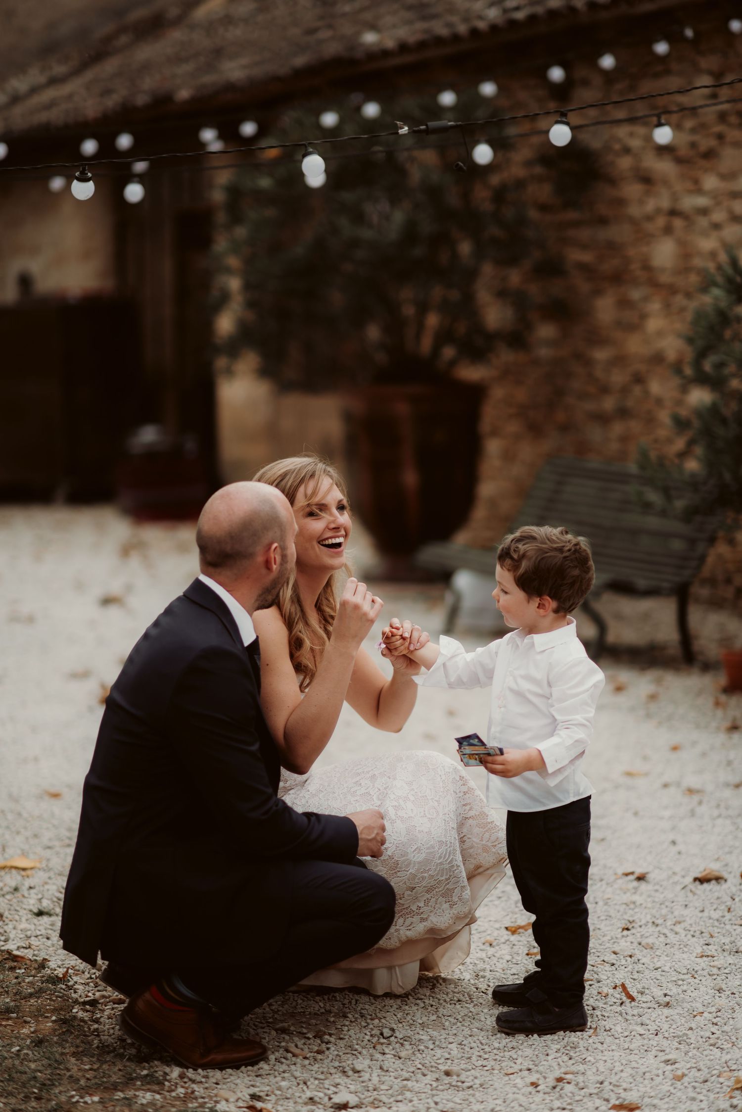 Heartwarming moment shared outside rustic stone venue with string lights overhead.