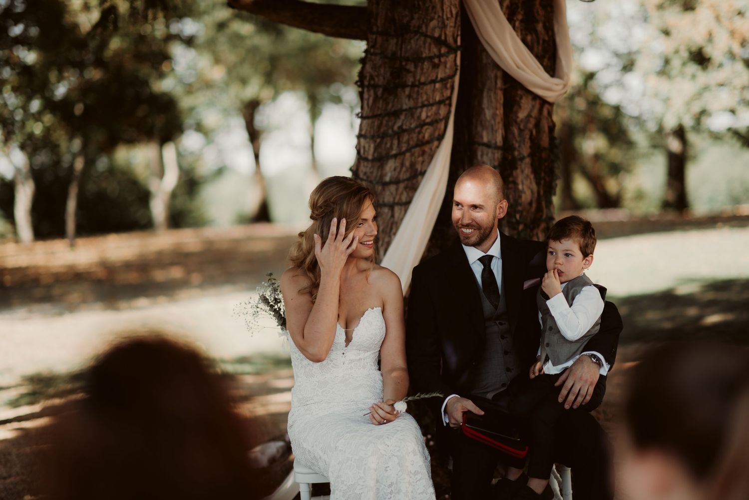 An emotional wedding ceremony moment captured under sunlit trees.