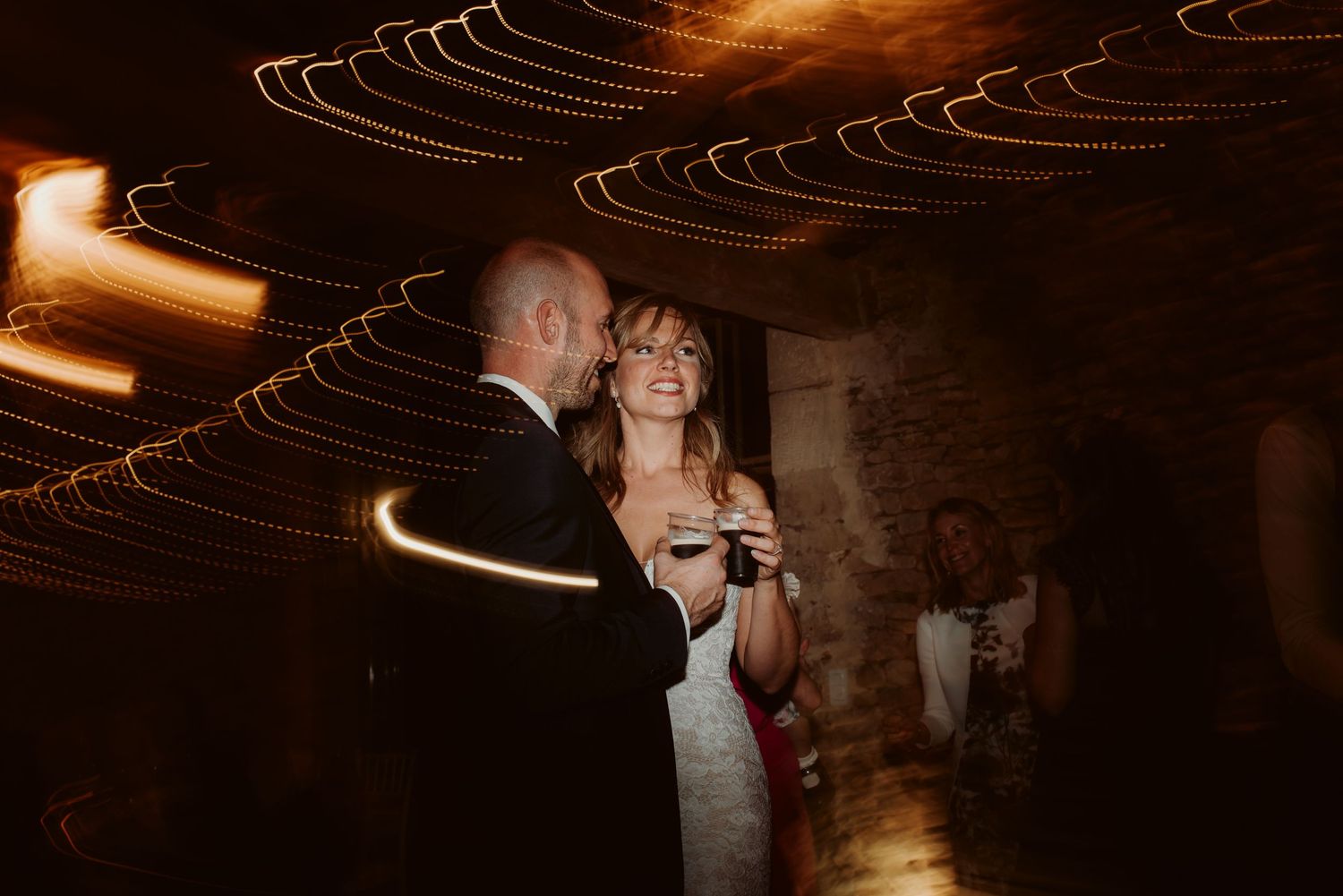 Couple dancing together under artistic light trails in a rustic venue.