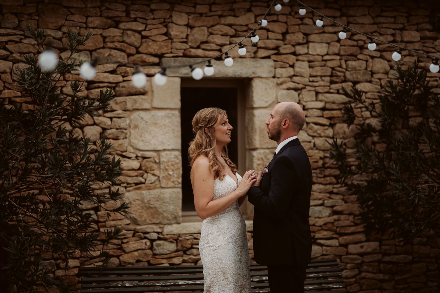 Wedding couple shares an intimate moment against a rustic stone wall with an arched doorway.