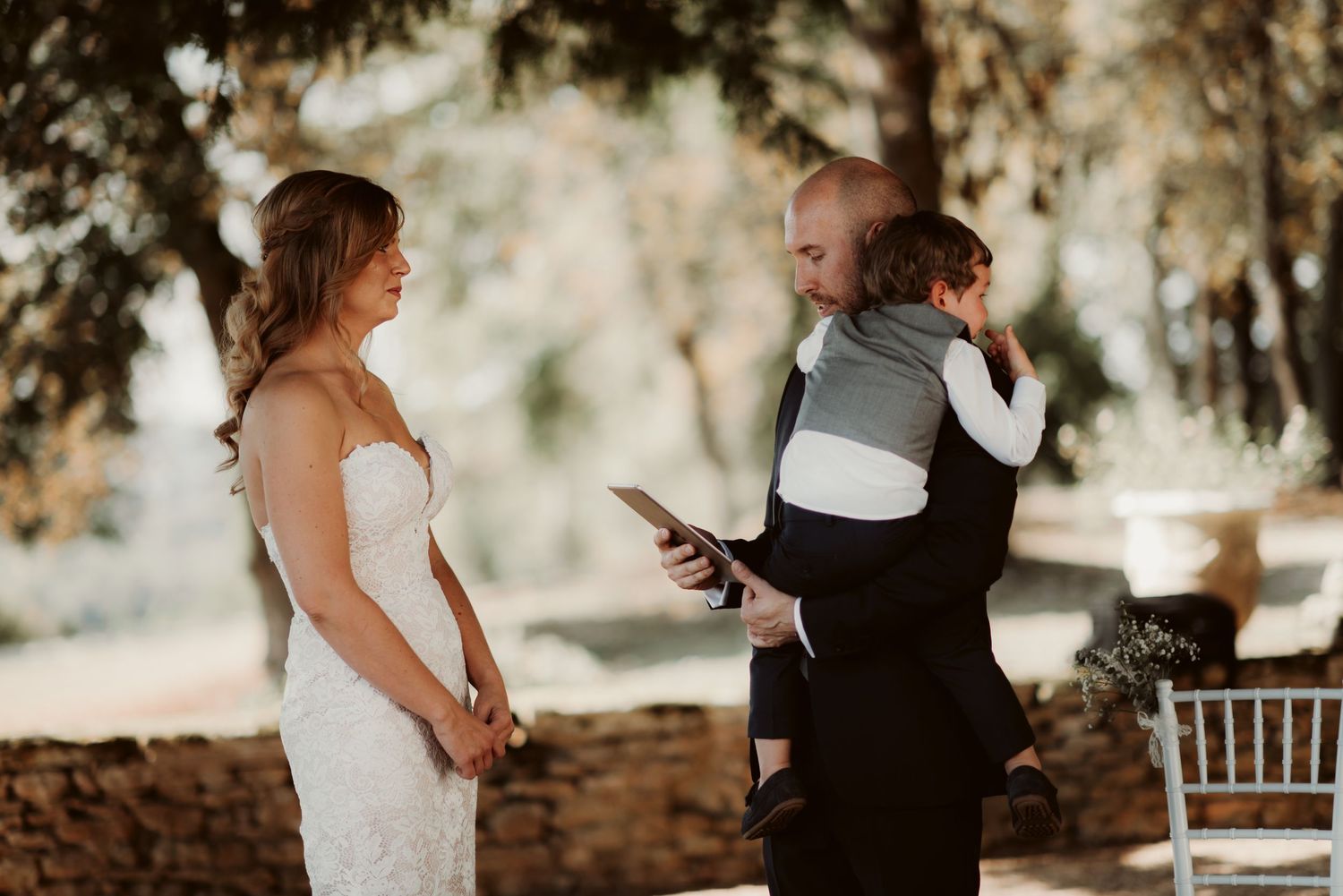 An outdoor wedding ceremony where a child is being held during the vows exchange.
