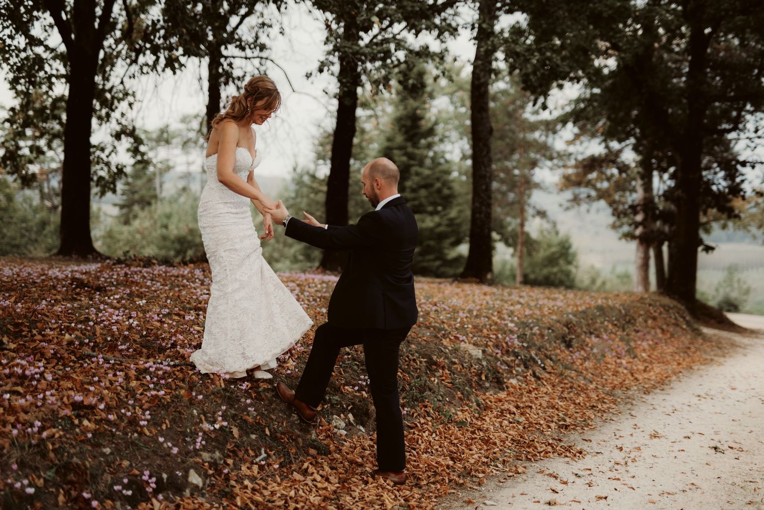 A couple shares a playful moment on a leaf-covered path in the woods.