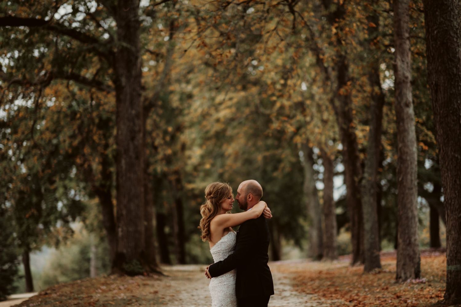 Wedding couple embraces on a romantic autumn path surrounded by golden trees.