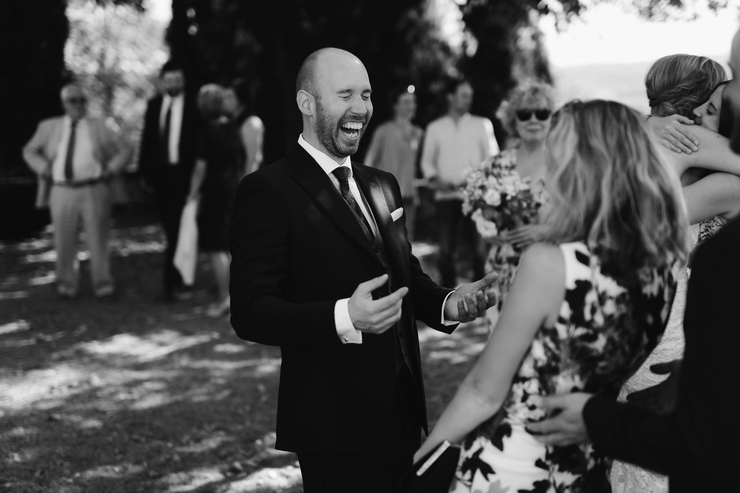 A black and white photo shows a joyful moment during an outdoor wedding celebration.