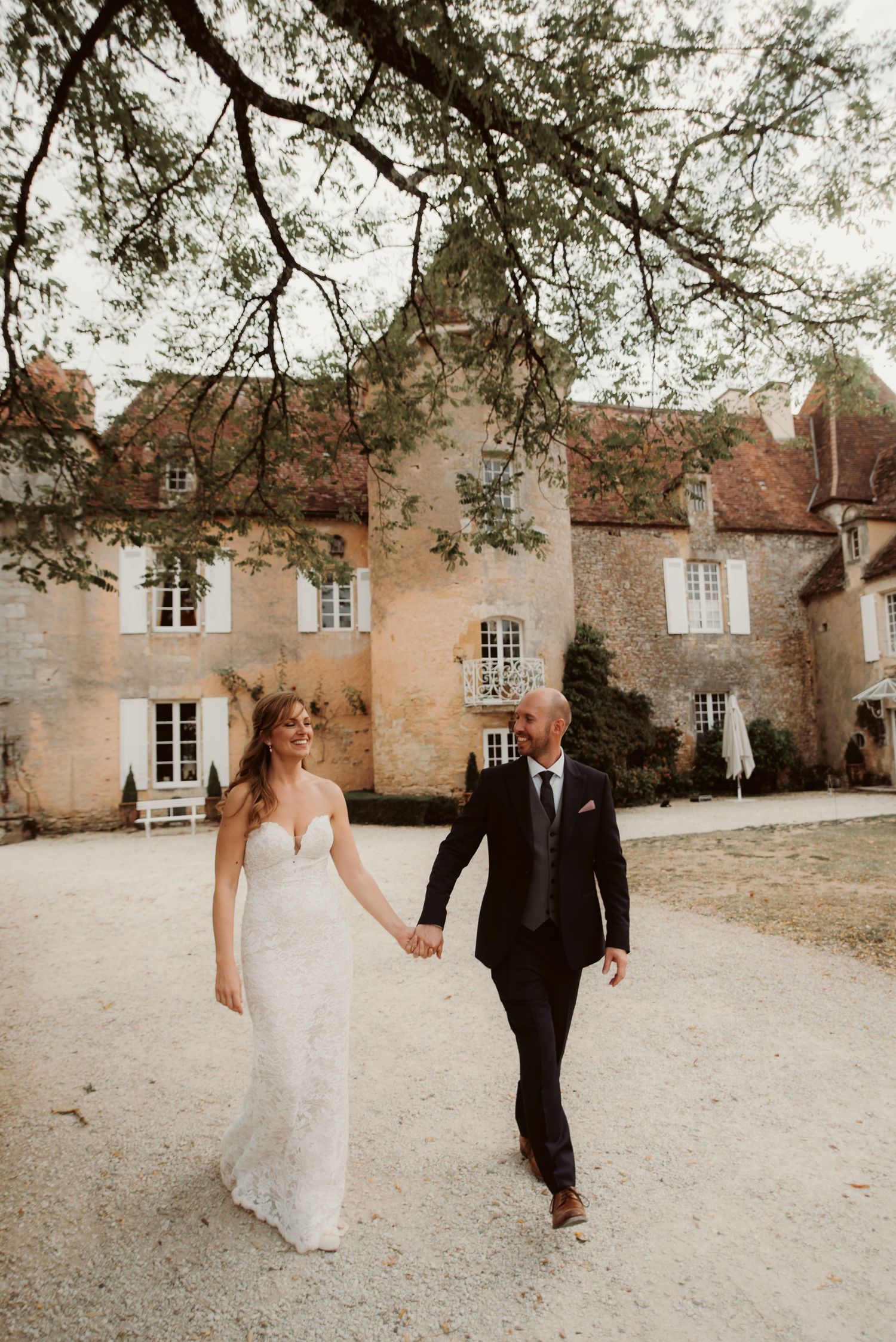Couple walks together on gravel path in front of an elegant historic chateau.