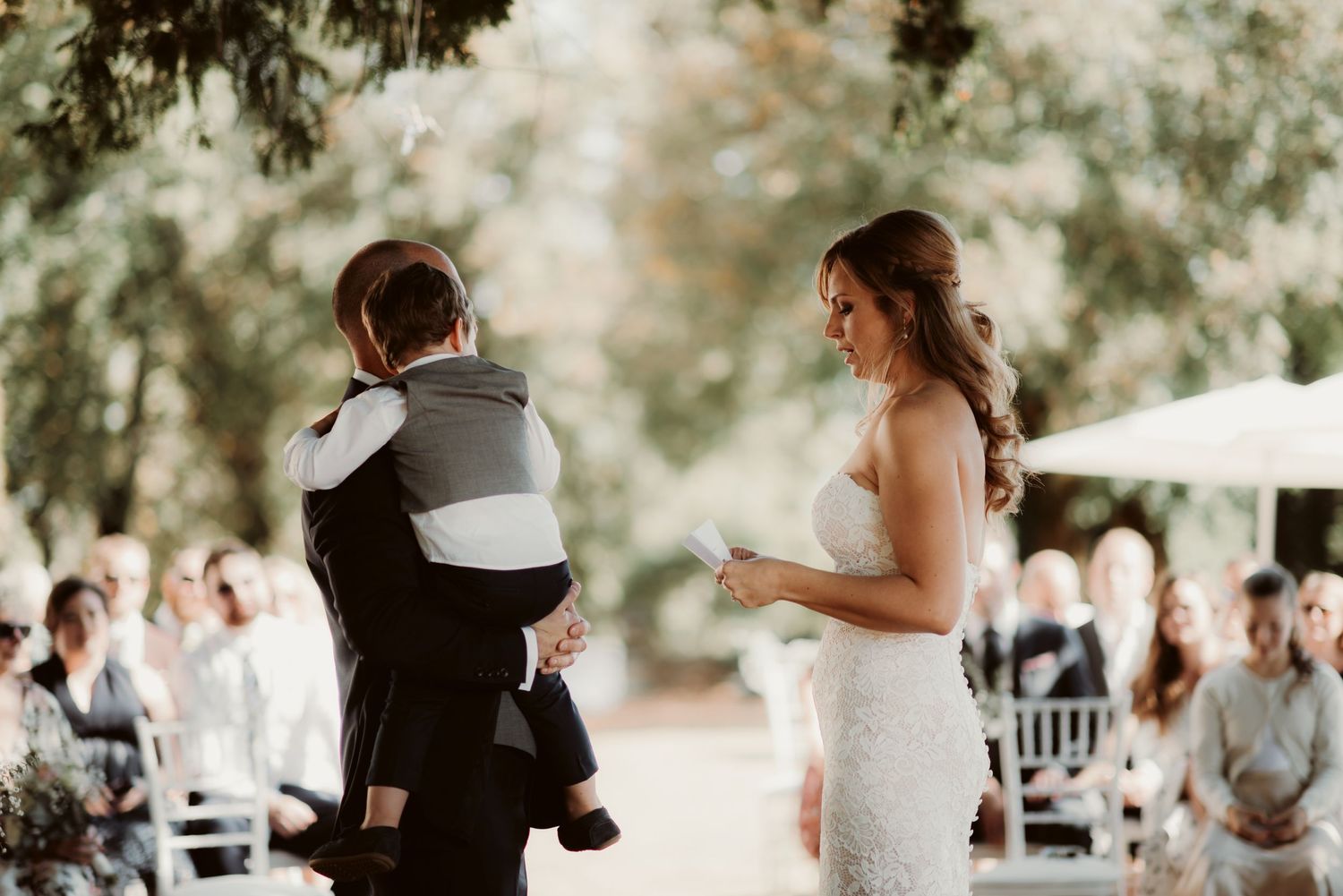 An emotional outdoor wedding ceremony with a child being held during the exchange of vows.