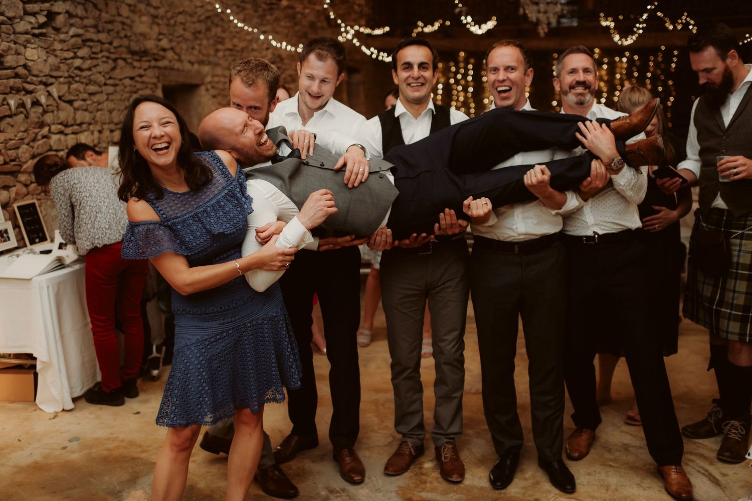 Reception guests share laughter and drinks during wedding celebrations in a stone-walled venue.