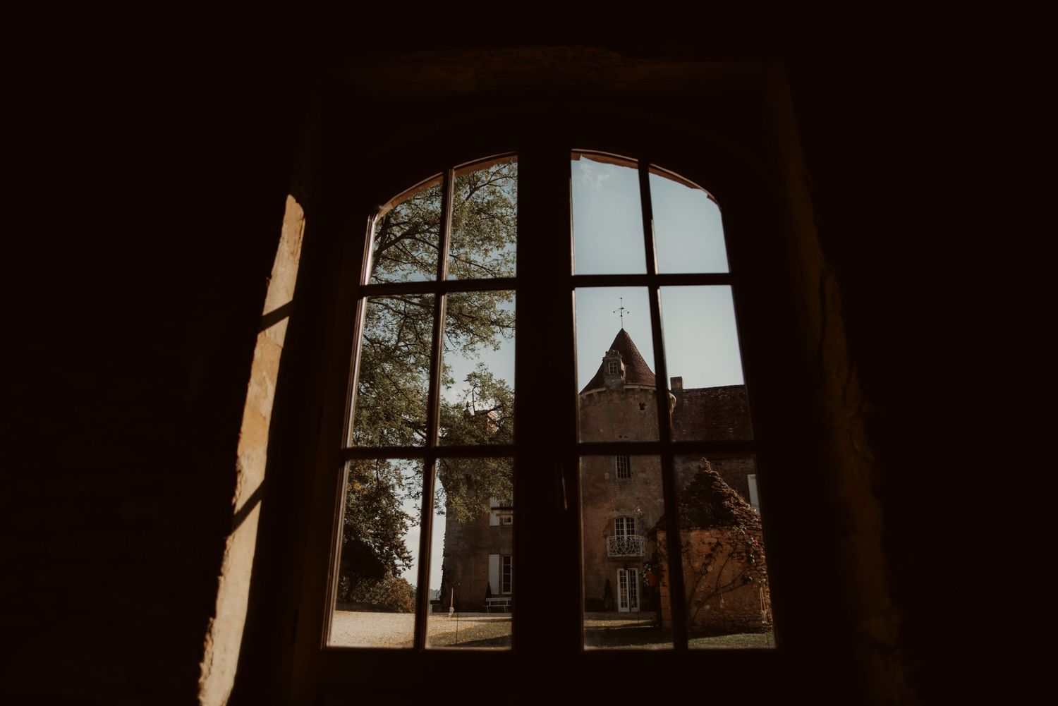 Arched window frame offering view of gothic architecture and trees in daylight.