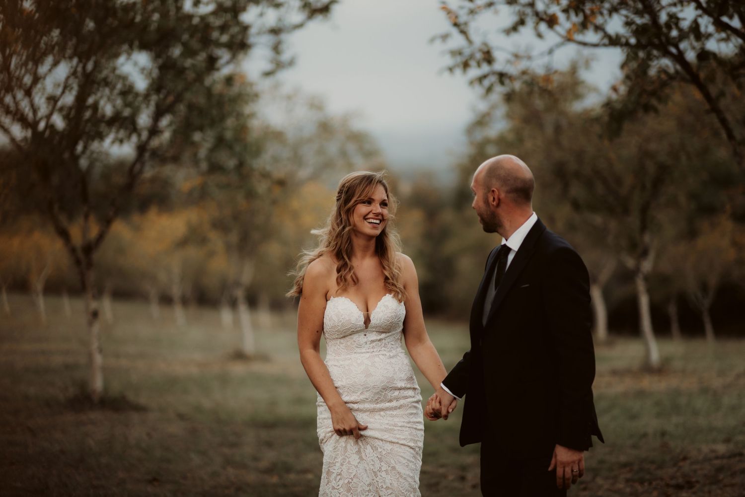A beautiful outdoor wedding portrait featuring a couple sharing a moment among trees at dusk.