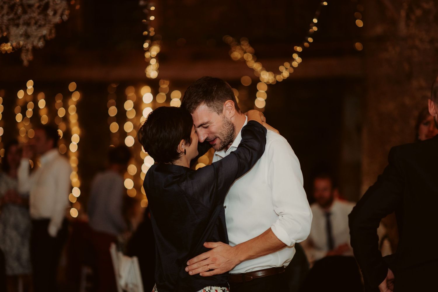 Couple shares an intimate dance moment under warm string lights at a wedding reception.