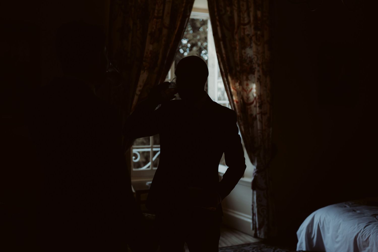 Dark silhouette against window with dramatic lighting and heavy curtains in interior setting.