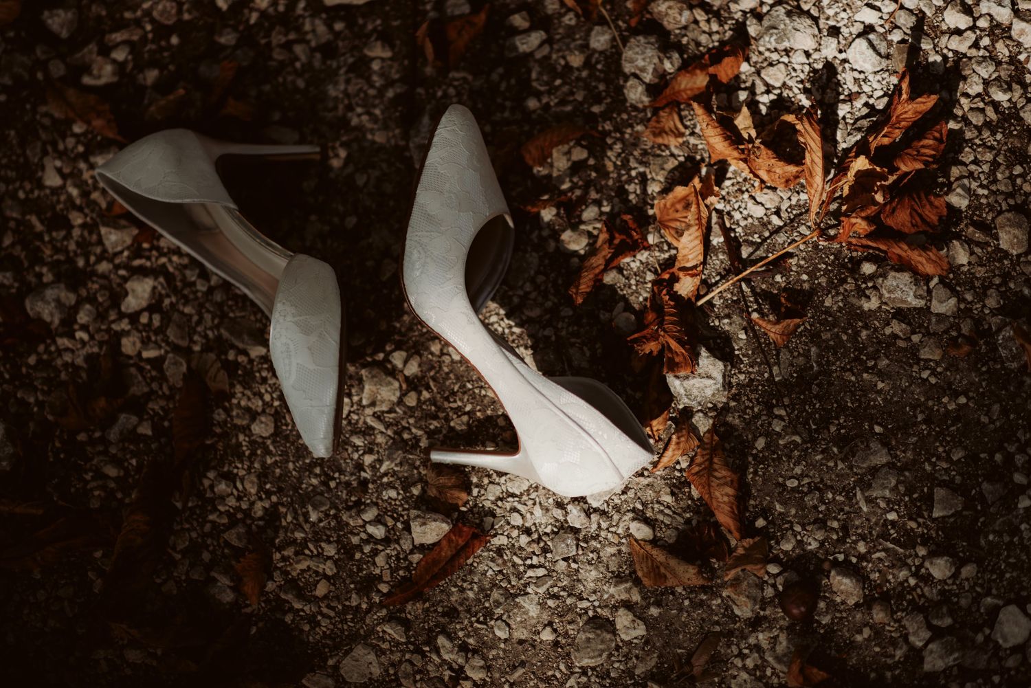 White bridal heels and autumn leaves arranged on dark textured ground.