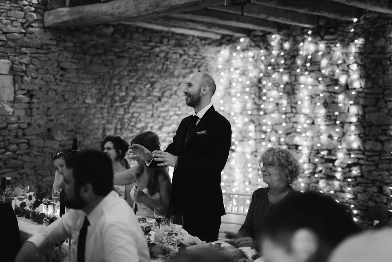 Reception dinner speech in a rustic stone venue with fairy light decorations.