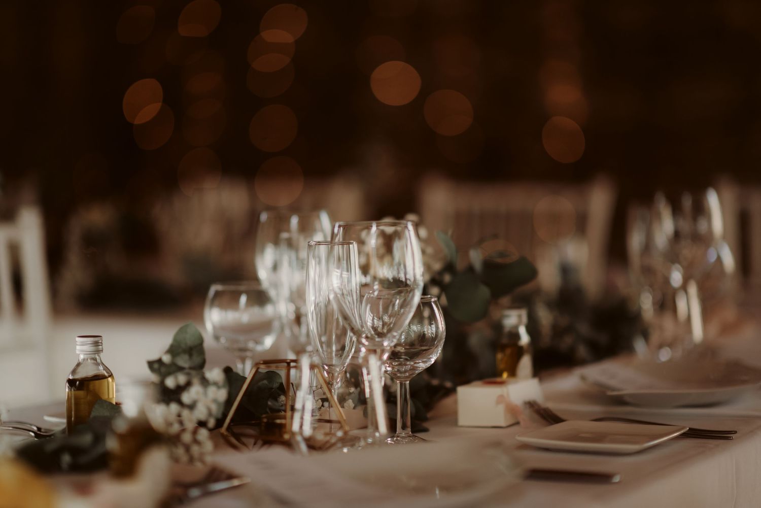 Atmospheric wedding table setup with wine glasses and place settings in warm lighting.