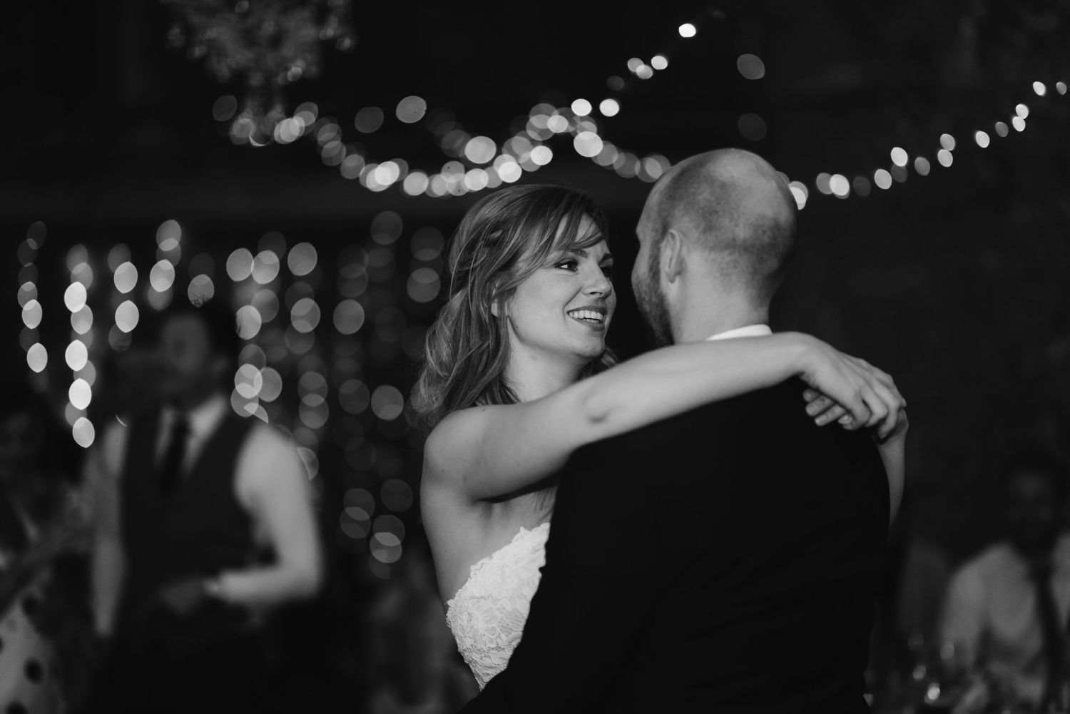 A black and white photo of a couple dancing with twinkle lights in the background.
