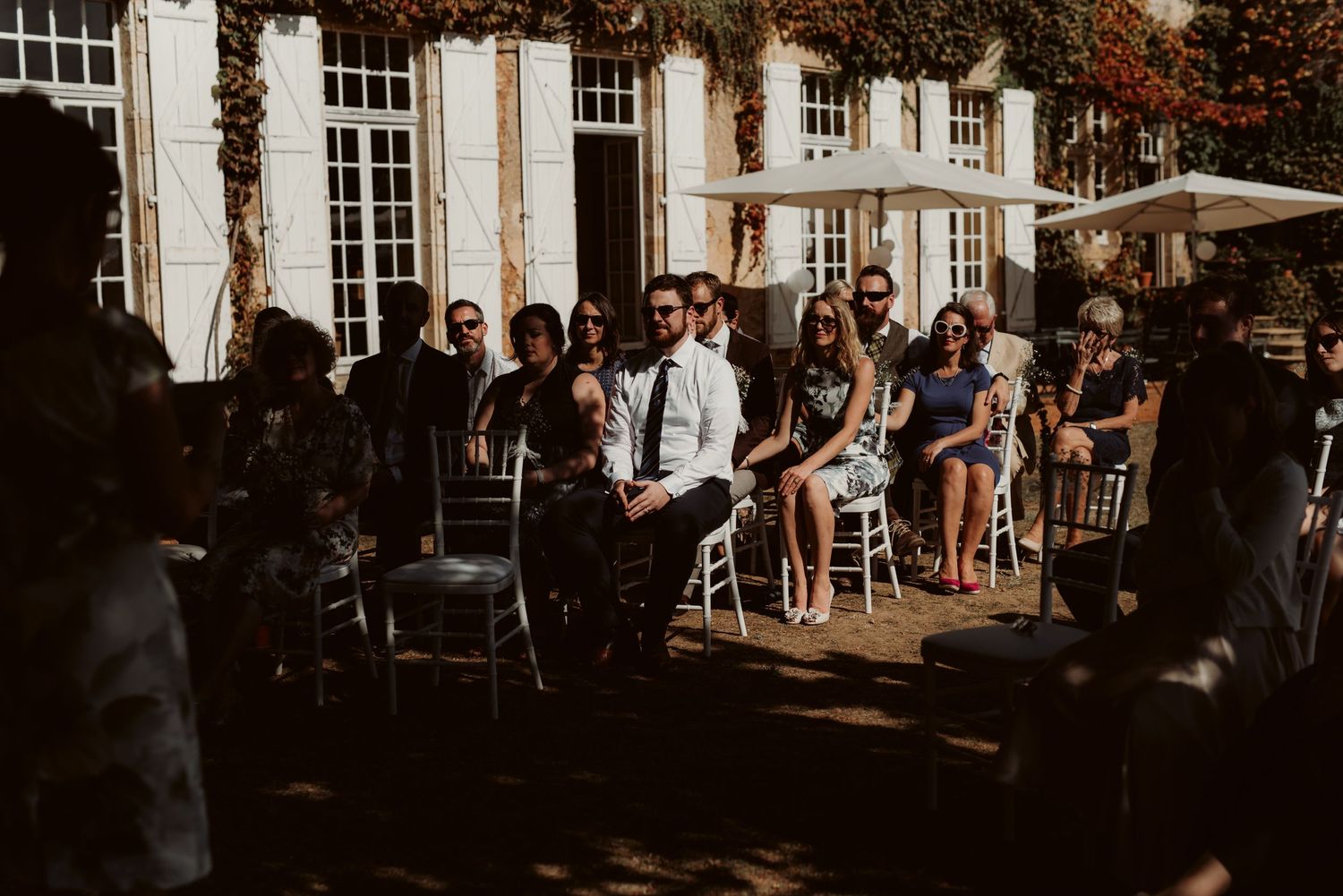 Wedding guests seated in chairs during an outdoor ceremony near a grand building.