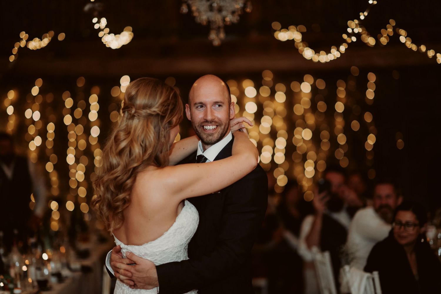 A couple embraces during their wedding dance under romantic string light decorations.