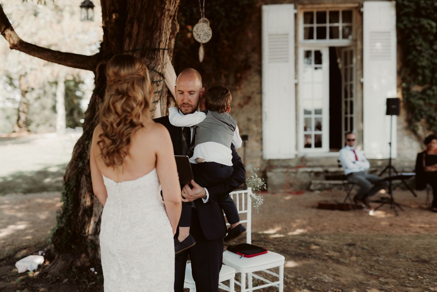 An intimate outdoor wedding ceremony in front of a rustic white building.