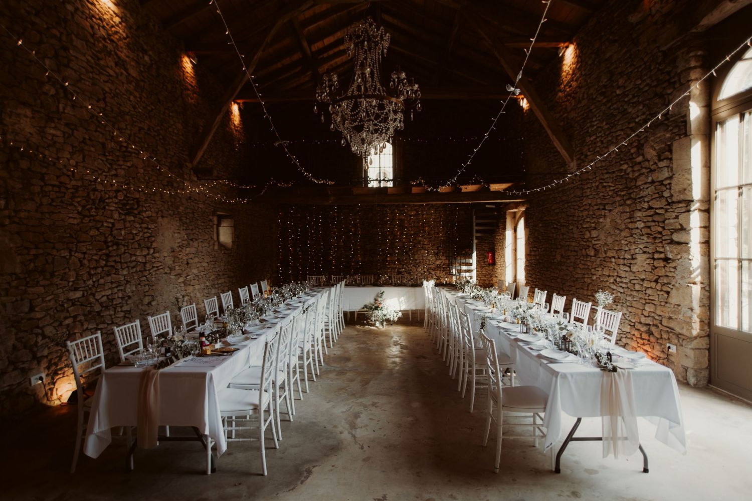 Elegant banquet setup with white tablecloths and chairs in a historic stone building with ambient lighting.