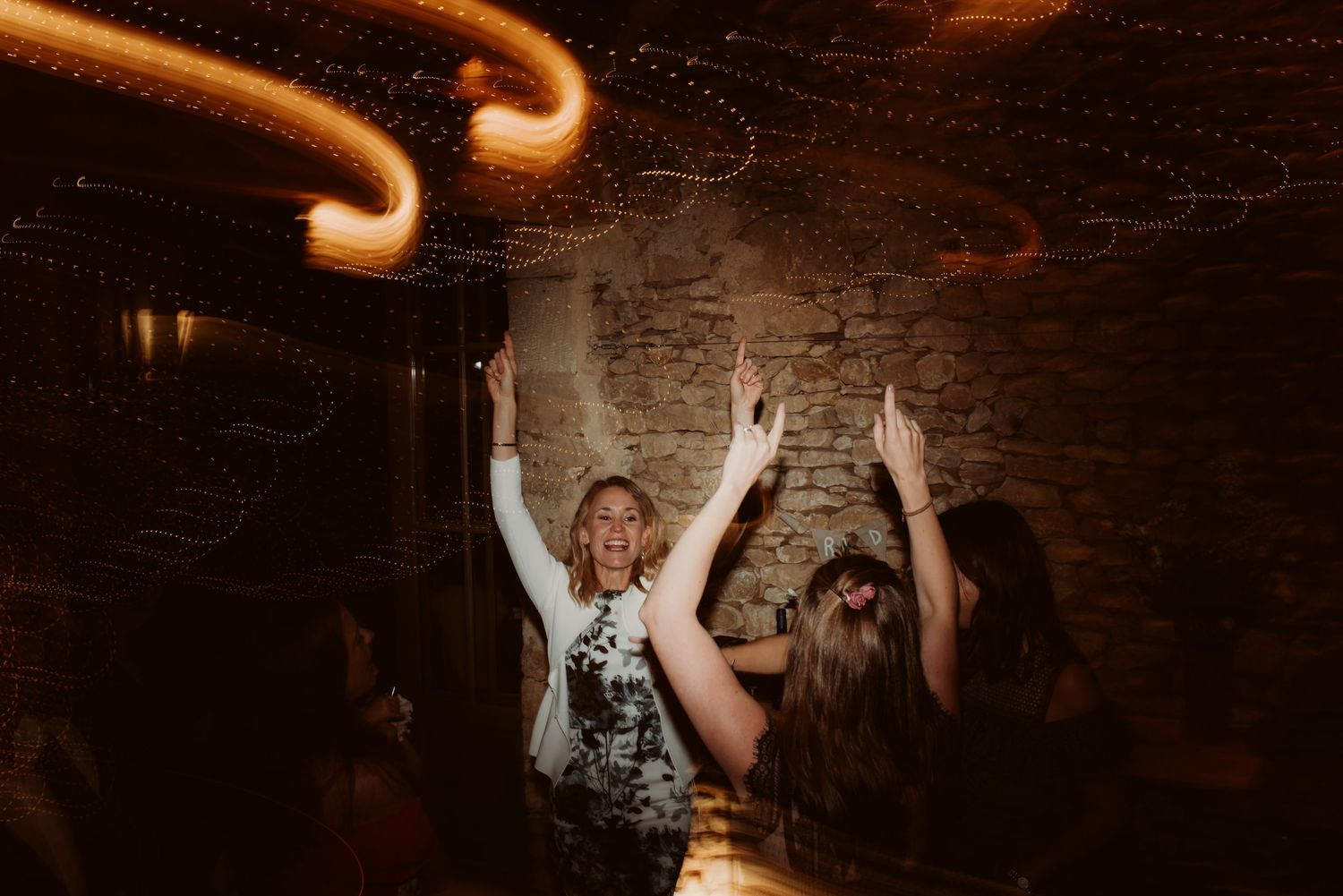 Wedding guests dance energetically under swirling orange light trails.