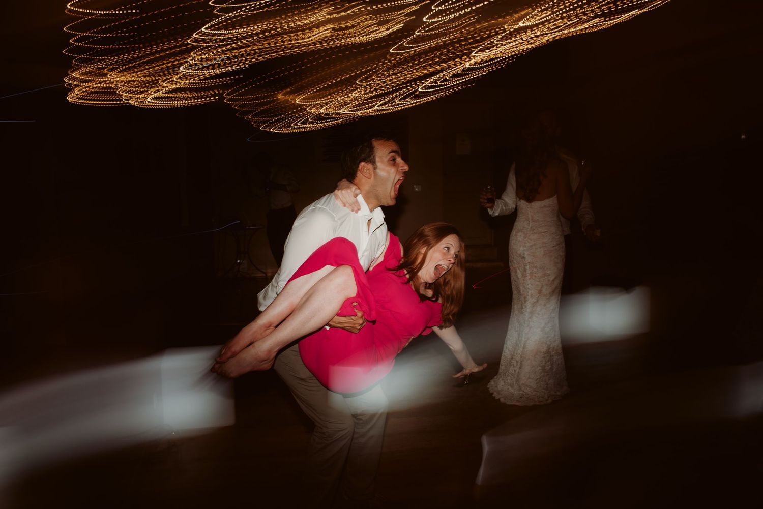 Guests dance under string lights during a lively wedding reception celebration.