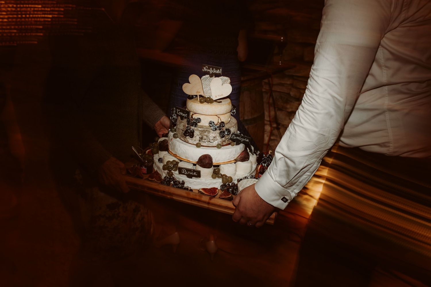 Someone carefully carries a three-tiered wedding cake in low lighting.