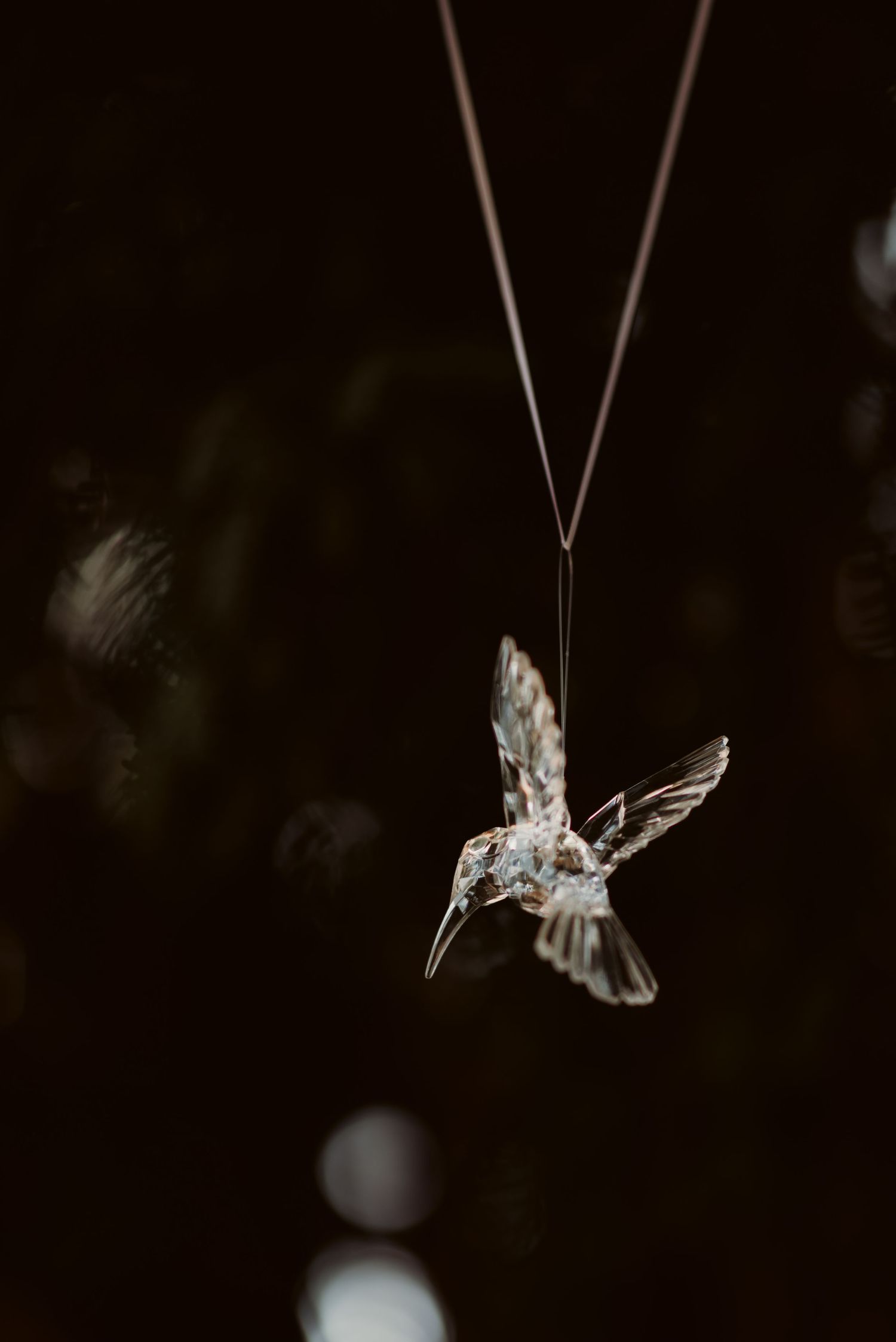 Delicate silver hummingbird necklace pendant against dark background.