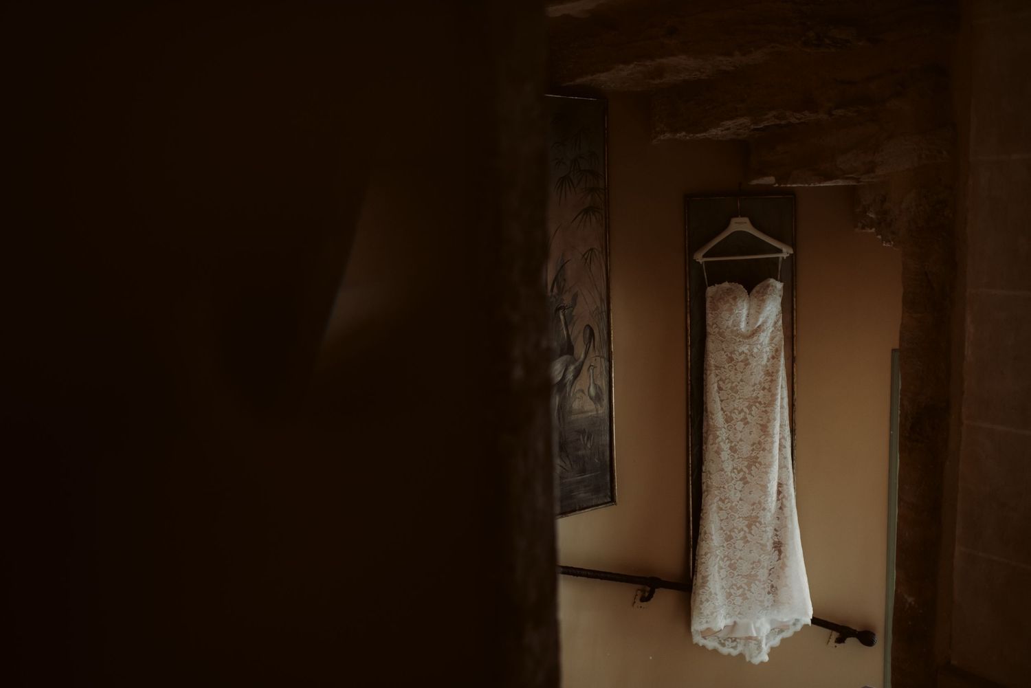 White wedding dress hanging in dimly lit doorway creates atmospheric silhouette.