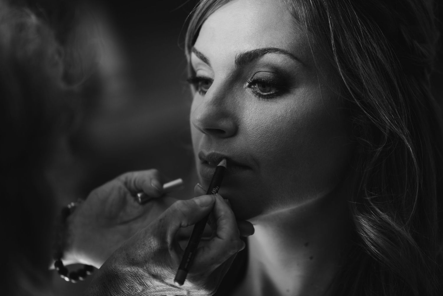Artistic black and white close-up of makeup application during wedding preparations.