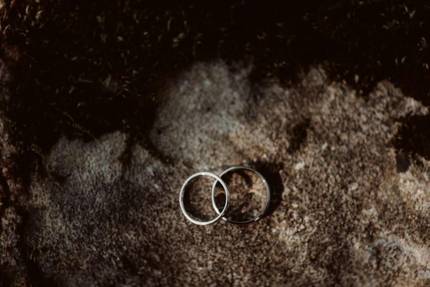 Two wedding rings photographed on rough stone surface with moody lighting.