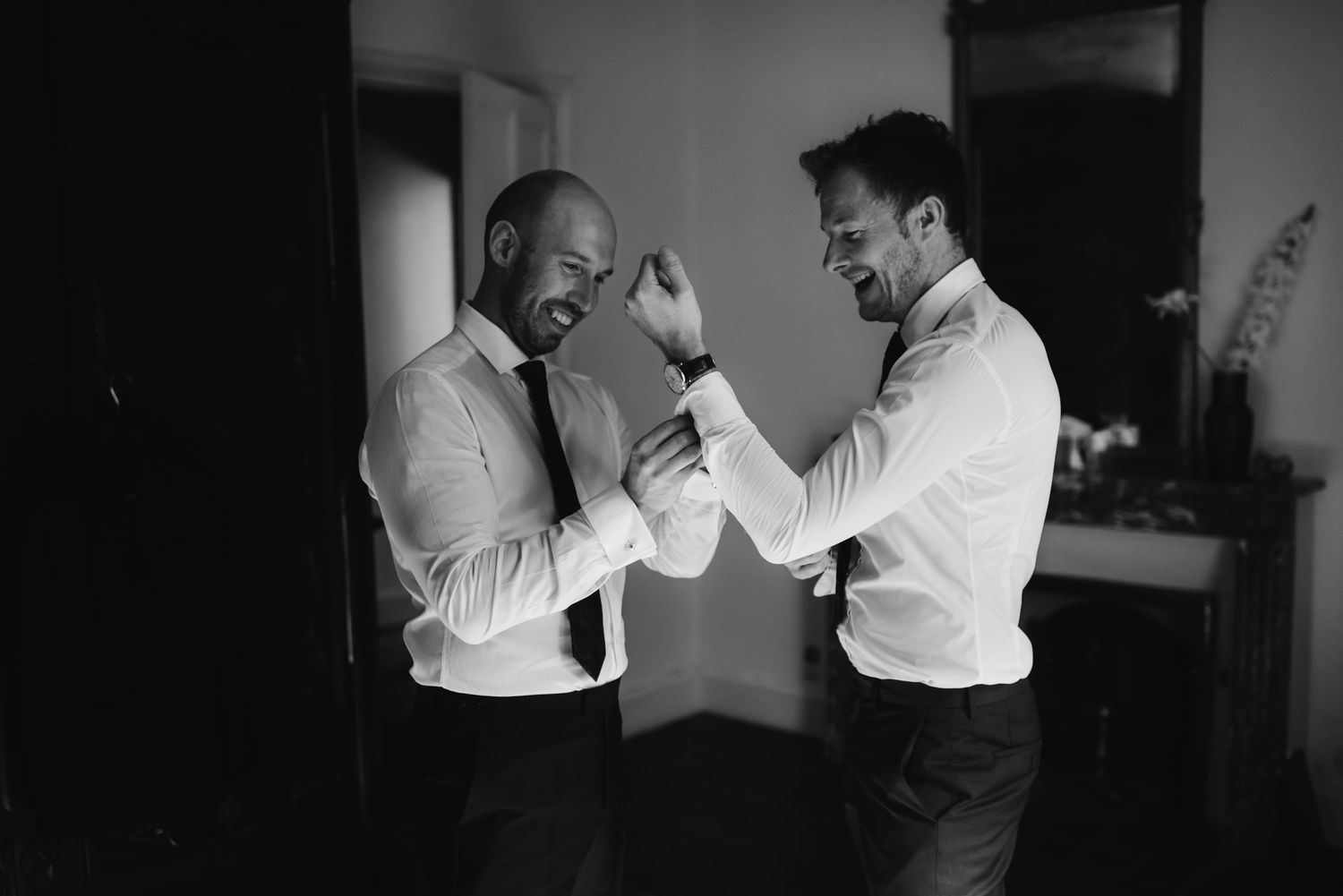 Black and white photo of two men in dress shirts adjusting their formal wear.