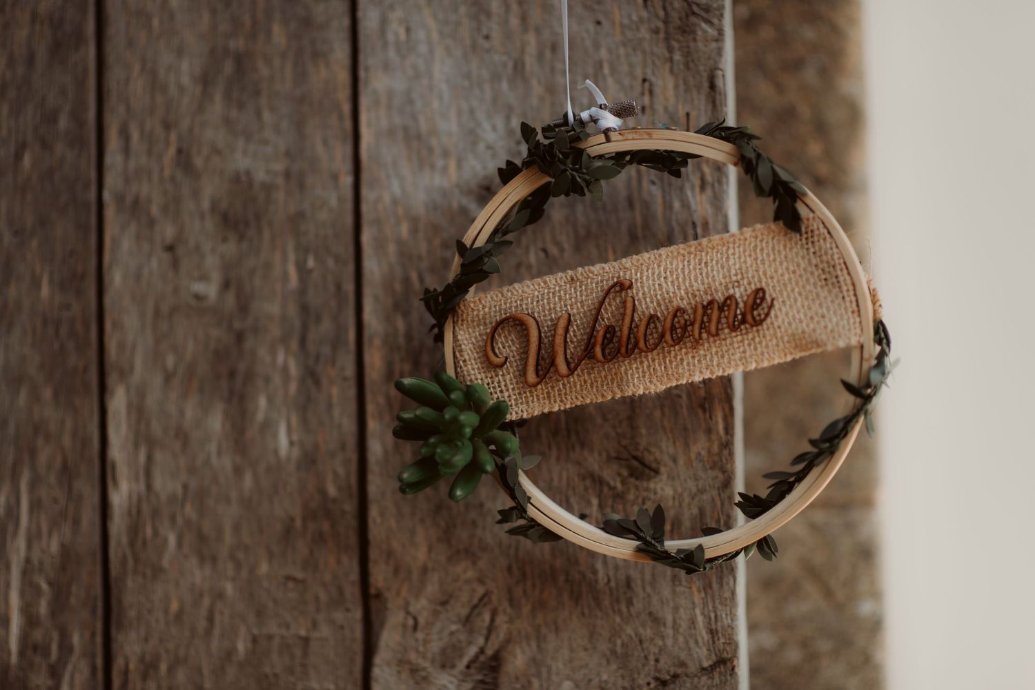 Rustic wooden welcome sign wrapped in twigs and greenery mounted on weathered wall.