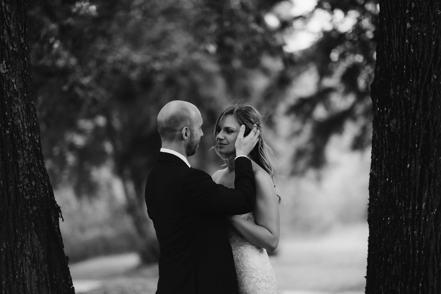 An intimate black and white portrait of newlyweds embracing among trees.