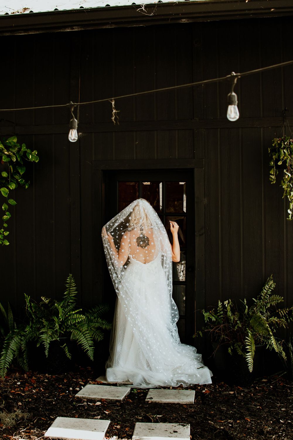 Atmospheric photo of a bride in a lace dress against a dark wooden backdrop with string lights.