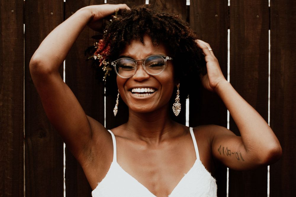 A joyful portrait showing natural curly hair and glasses against a light background.