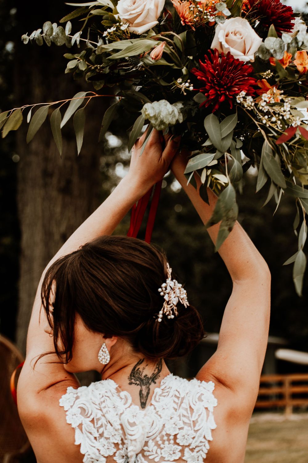 Bride holding colorful autumn bouquet overhead showing intricate lace dress details.