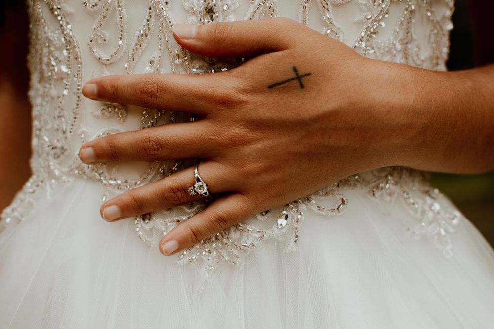 Close-up of hands touching intricate beadwork details on a white wedding dress.