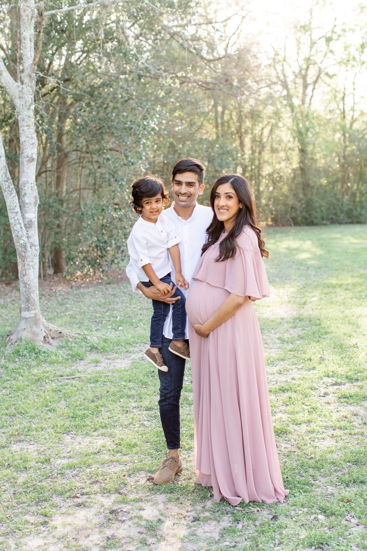 A family poses for a portrait in a sunlit park setting with birch trees in the background.