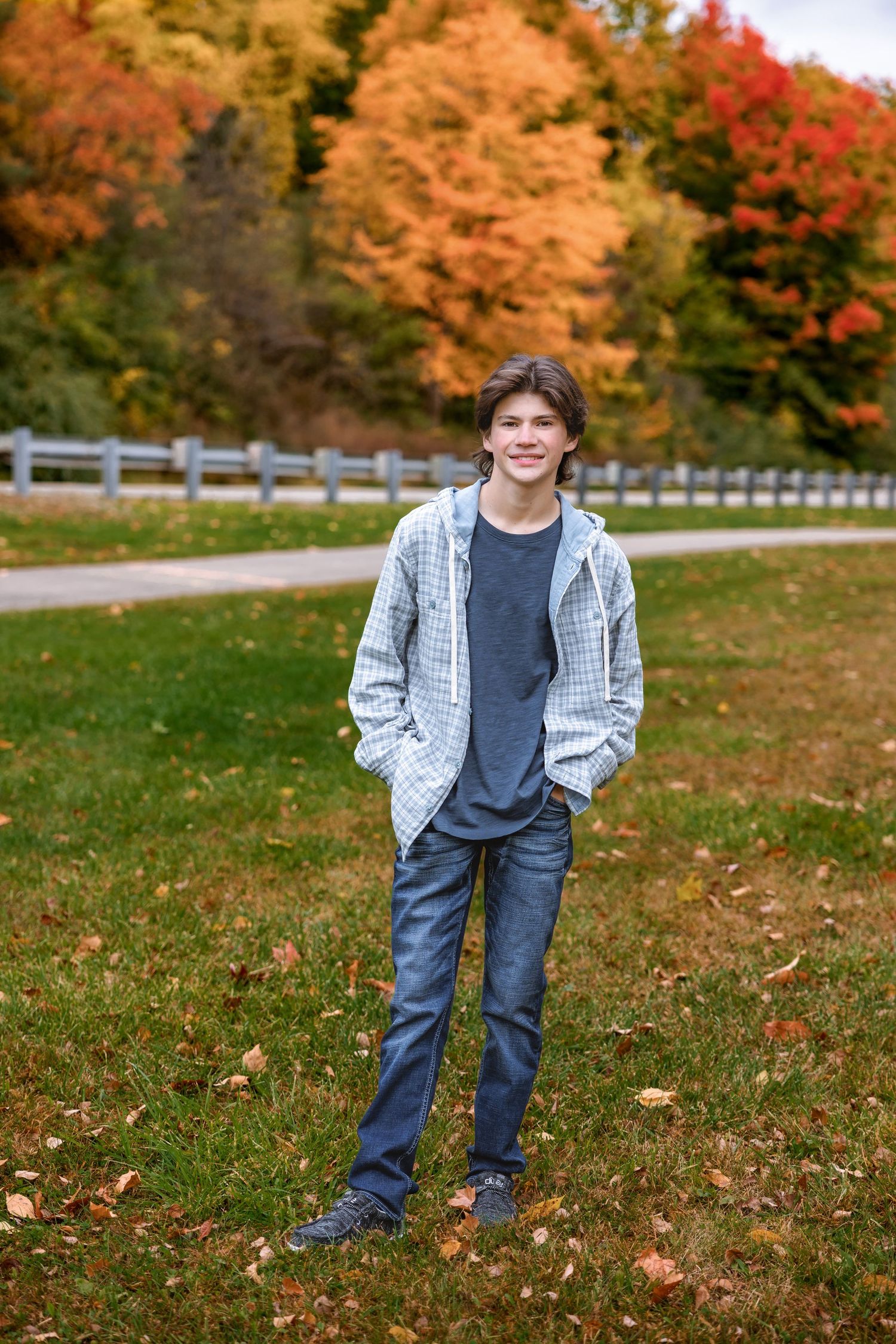 Casual portrait against backdrop of vibrant fall foliage and white fence.