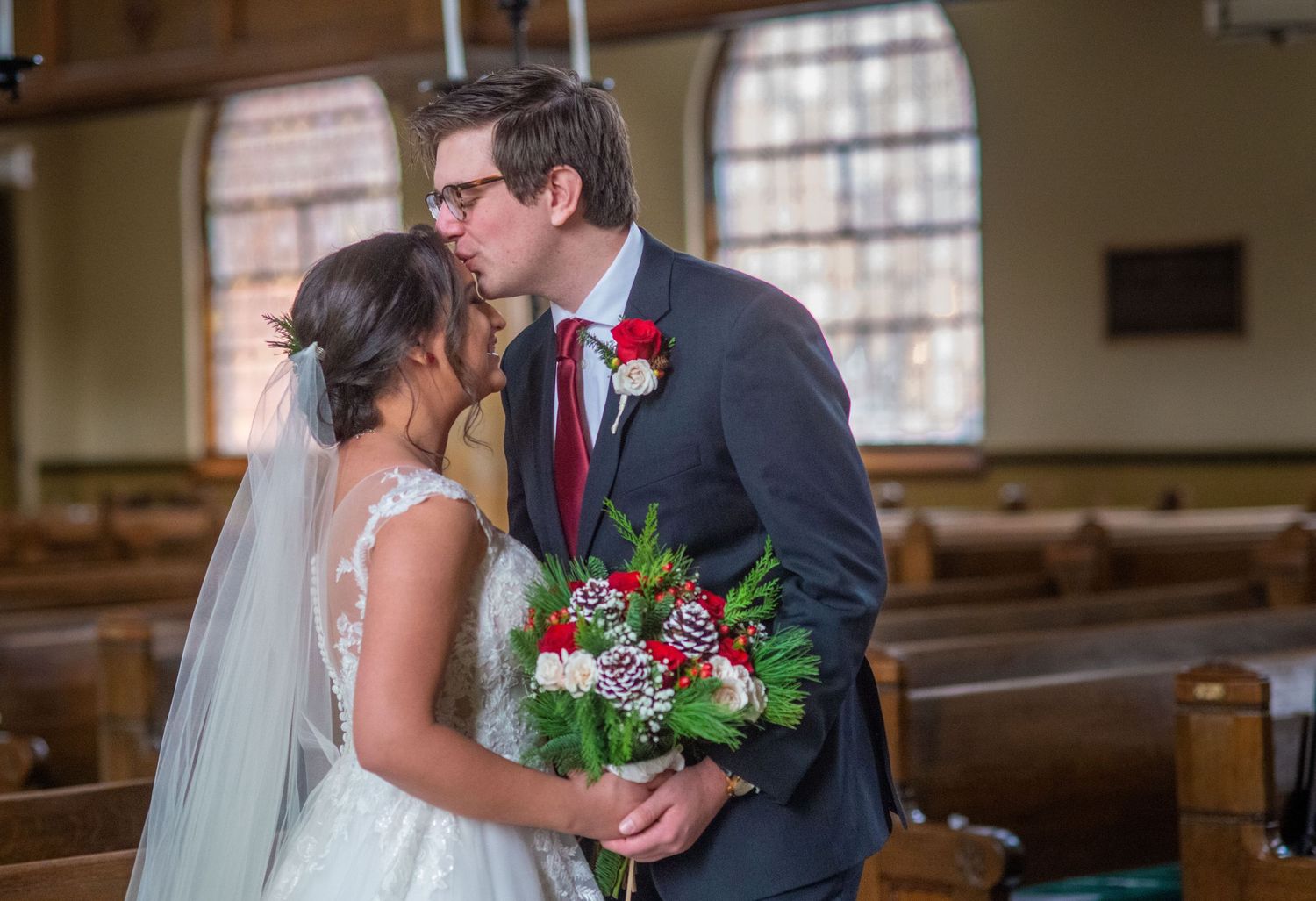A romantic moment captured between newlyweds in a church with wooden pews and arched windows.